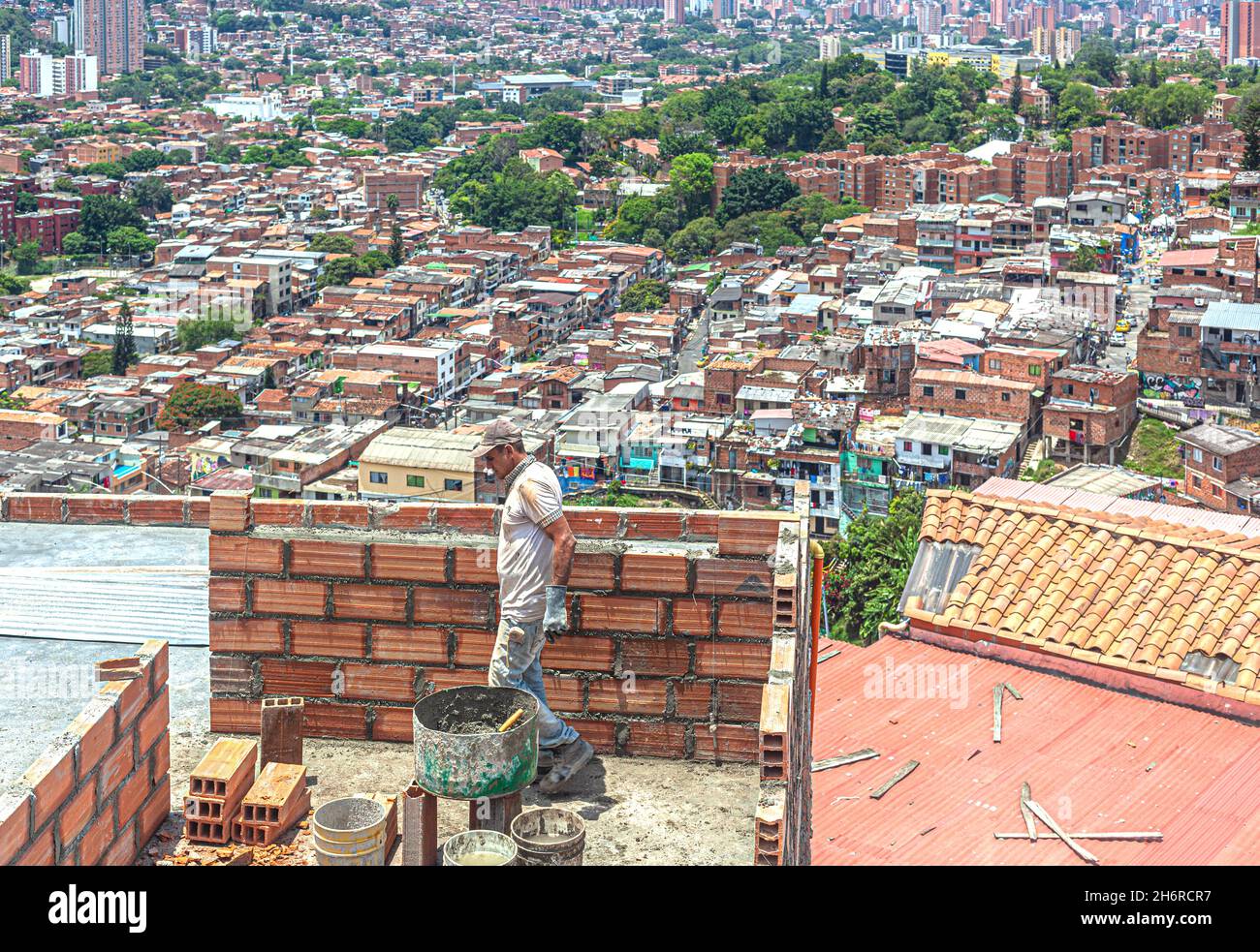 Muratore al lavoro sulla cima di una casa che domina la città, Comuna 13, Medellin, Colombia. Foto Stock