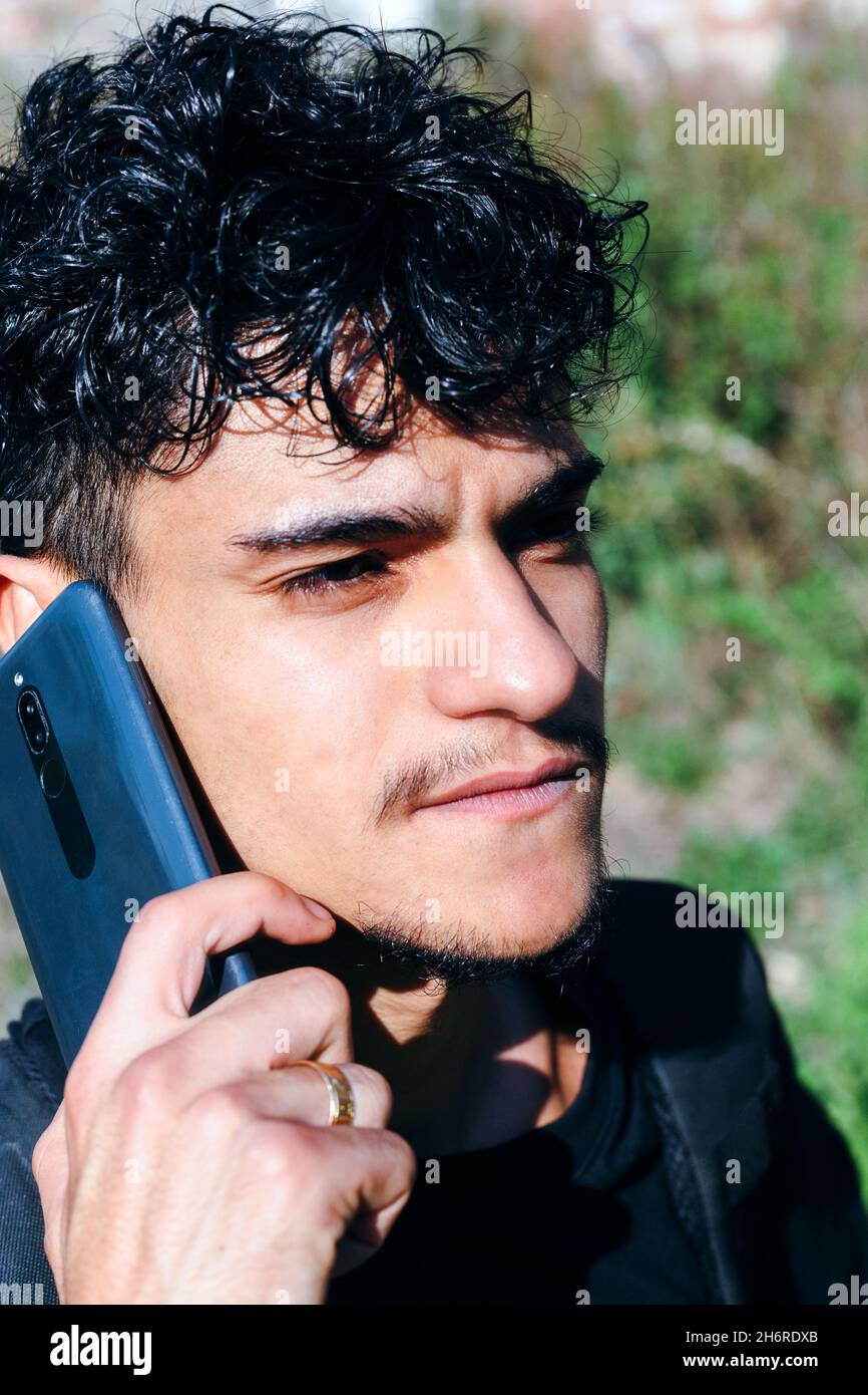 Ritratto di un giovane che parla sul suo smartphone. Immagine esterna di un giovane uomo con capelli ricci che parla sul suo cellulare - primo piano. Foto Stock