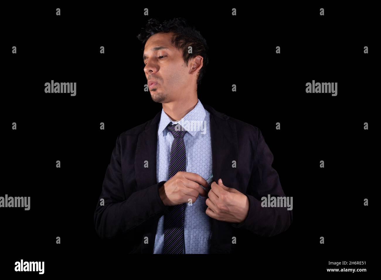 L'uomo d'affari tiene i soldi in tasca mentre fischiando slyly, isolato su sfondo nero. Giovane adulto latino giovane. Foto Stock