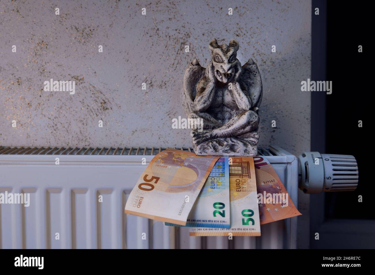 Una moderna batteria di riscaldamento a casa con rubinetto spento, banconote in euro e una chimera seduta su di loro. Foto Stock