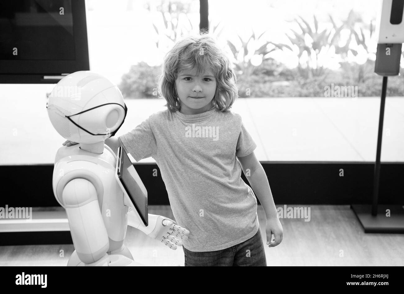 bambino e assistente robot con schermo informativo in maschera protettiva. futuro pandemico robotico Foto Stock