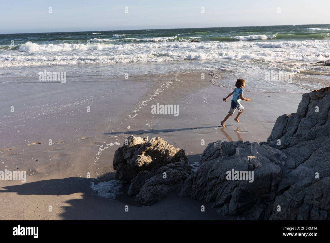 Un ragazzo che corre sulla sabbia a bordo dell'acqua su una spiaggia di sabbia. Foto Stock