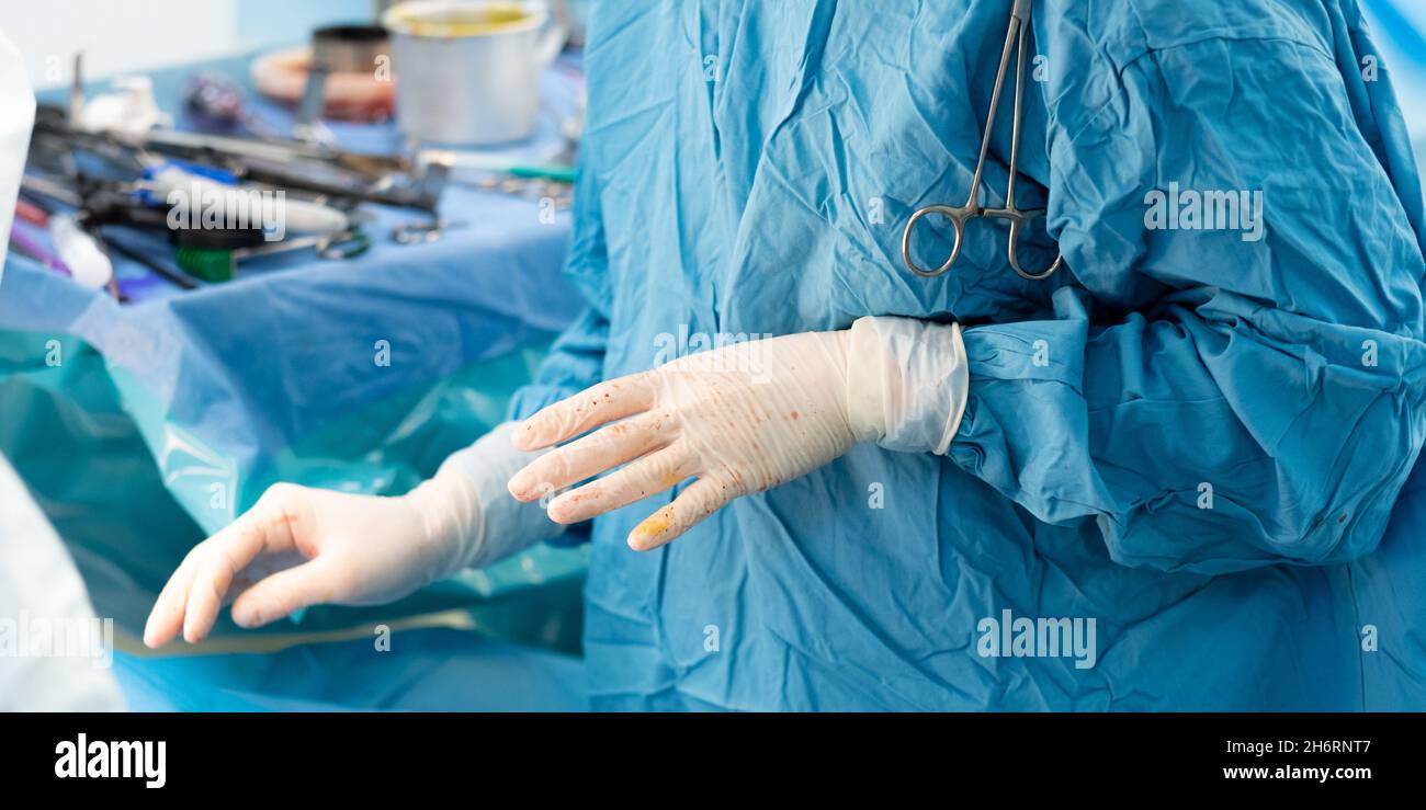 Focalizzazione selettiva sulle mani di un chirurgo in guanti chirurgici sterili durante l'intervento chirurgico sullo sfondo degli strumenti chirurgici. Foto Stock