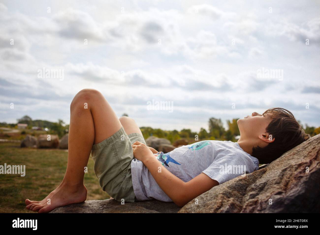 Un ragazzo giovane si adagia sulla roccia a piedi nudi sotto il sole Foto Stock