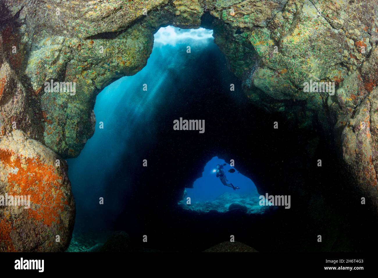 La luce del sole scola da un lucernario in cima a questa caverna al largo della costa di Kona della Big Island, Hawaii. Un subacqueo (MR) è incorniciato all'ingresso c Foto Stock