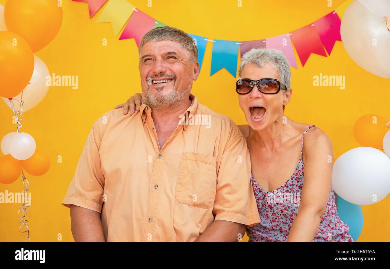 Coppia felice anziani su sfondo giallo con palloncini Foto Stock