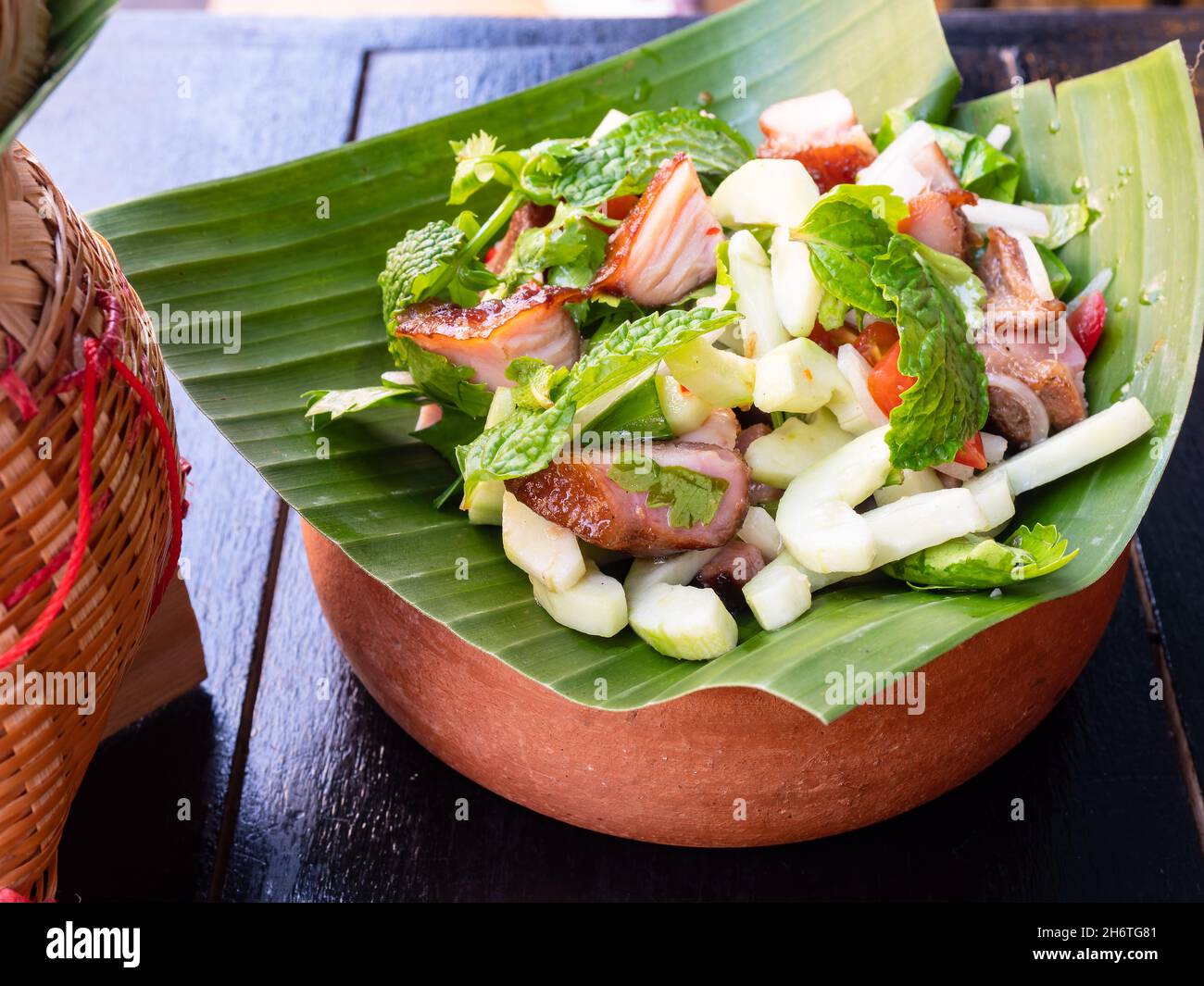Nam Tok Moo, cucina tradizionale tailandese con spalla di maiale alla griglia, succo di lime, foglie di menta, cetriolo, aglio e peperoncino serviti su una foglia di palma. Foto Stock