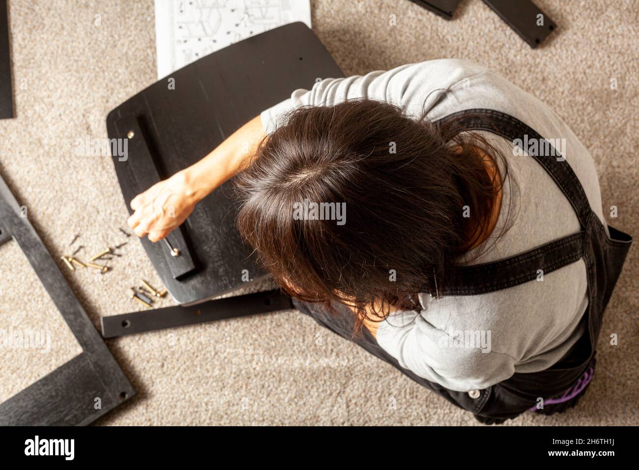 Concetto di assemblaggio di mobili fai da te che include una persona caucasica seduta su pavimento di moquette con pezzi di mobili, cercando di montarlo basato su istruttori Foto Stock