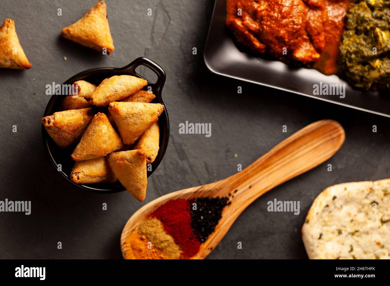 Primo piano immagine di un tavolo con piatti deliziosi provenienti dall'India. Fondo scuro chiaro con naan, pollo al curry, paneer al palak, samosa, varie spezie A. Foto Stock