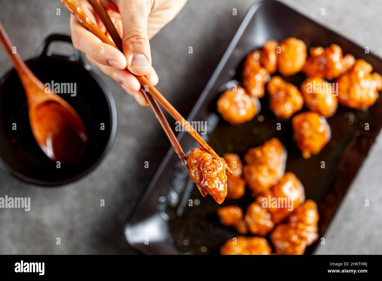 Una persona sta mangiando il pollo d'arancia del mandarino delizioso, un piatto americano cinese usando i bastoncini di legno. La salsa viene servita in una ciotola di porcellana. bac. Scuro Foto Stock
