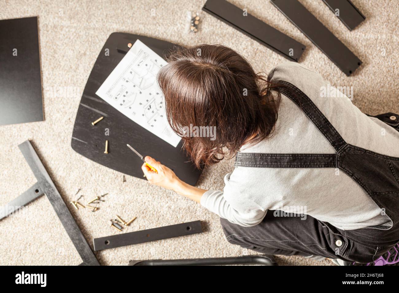 Concetto di assemblaggio di mobili fai da te che include una persona caucasica seduta su pavimento di moquette con pezzi di mobili, cercando di montarlo basato su istruttori Foto Stock