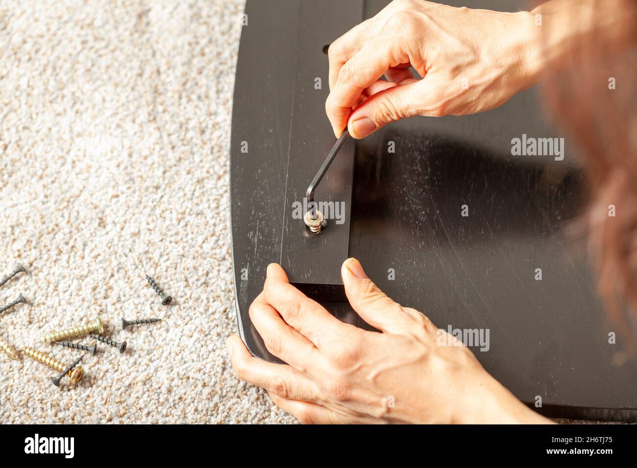 Concetto di assemblaggio di mobili fai da te che include una persona caucasica seduta su pavimento di moquette con pezzi di mobili, cercando di montarlo. Utilizza la forma a L. Foto Stock