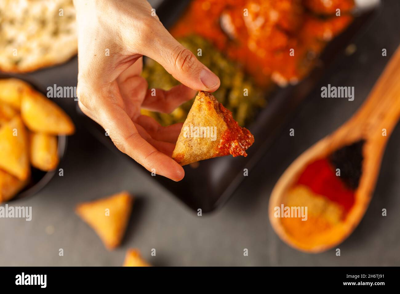 Una donna sta mangiando il cibo indiano delizioso con vari piatti. Lei immerge una samosa triangolare in curry. Concetto per mangiare cucina asiatica o ristorante w Foto Stock