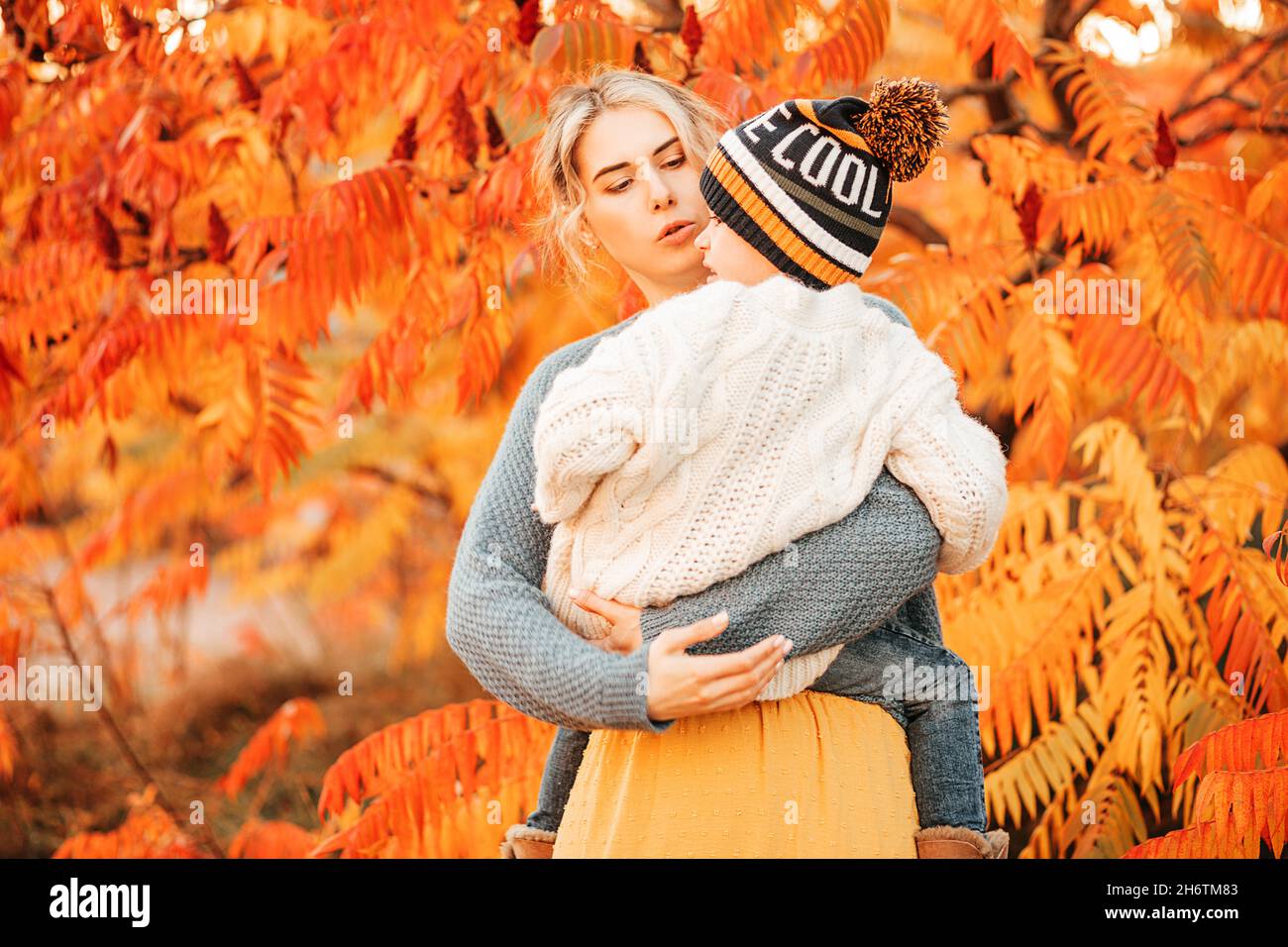 Ritratto di giovane donna che tiene il bambino in braccia su sfondo di verde rosso brillante - giallo autunno fogliame, parlando con lui, calmante. Il concetto di Foto Stock