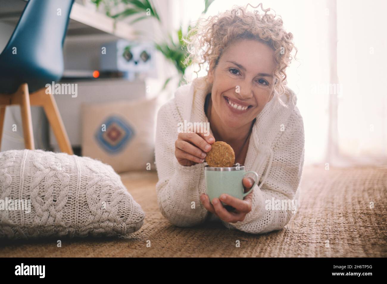 La giovane donna adulta felice fa colazione a casa adagiandosi sul tappeto  e mangiando dolci biscotti con caffè e latte sorridendo alla macchina  fotografica in una allegra pezza Foto stock - Alamy