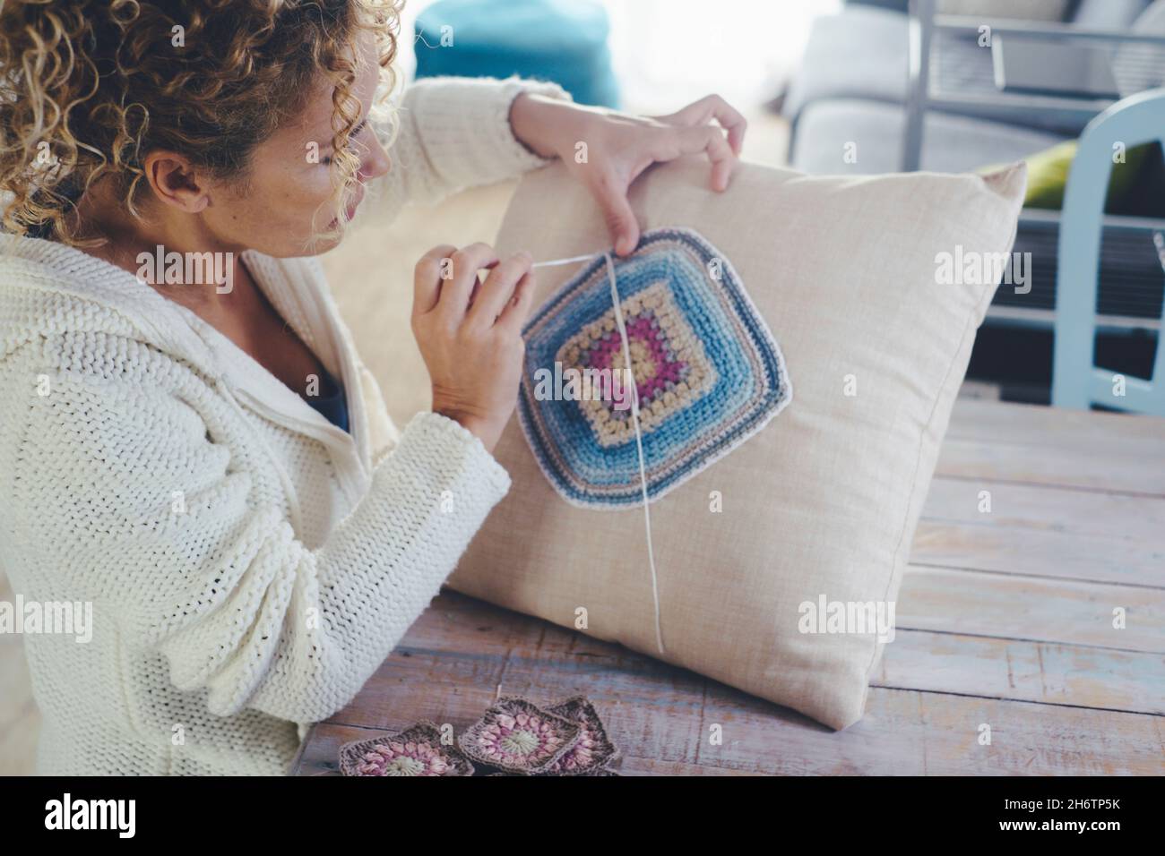 Donna a casa che fa lavoro a maglia o uncinetto su un cuscino bianco per decorare e produrre decorazioni. Le donne a casa sono occupate di hobby e leisu al coperto Foto Stock