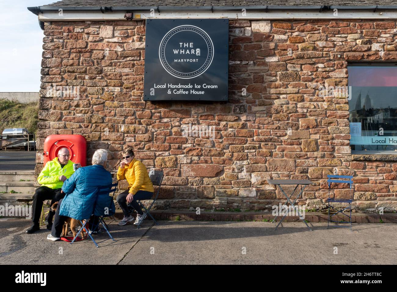 Tre persone seduti fuori dal Wharf Maryport, una caffetteria e gelateria accanto al porto di Marport in Cumbria, Regno Unito, durante il mese di novembre Foto Stock