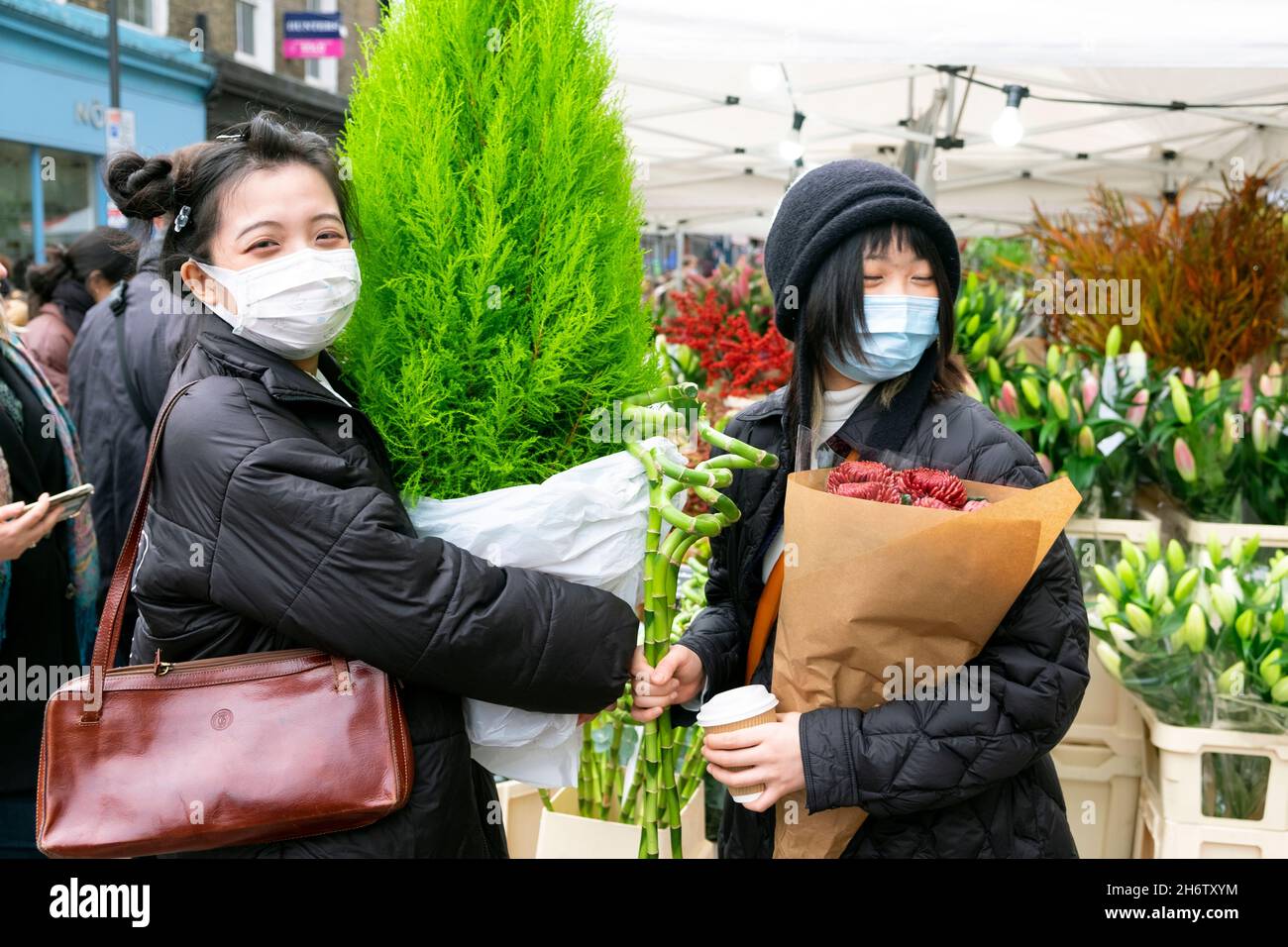 Columbia Road Flower Market giovani cinesi donne piante covid facemask facemask al mercato stalla in strada Novembre 2021 East London UK KATHY DEWITT Foto Stock