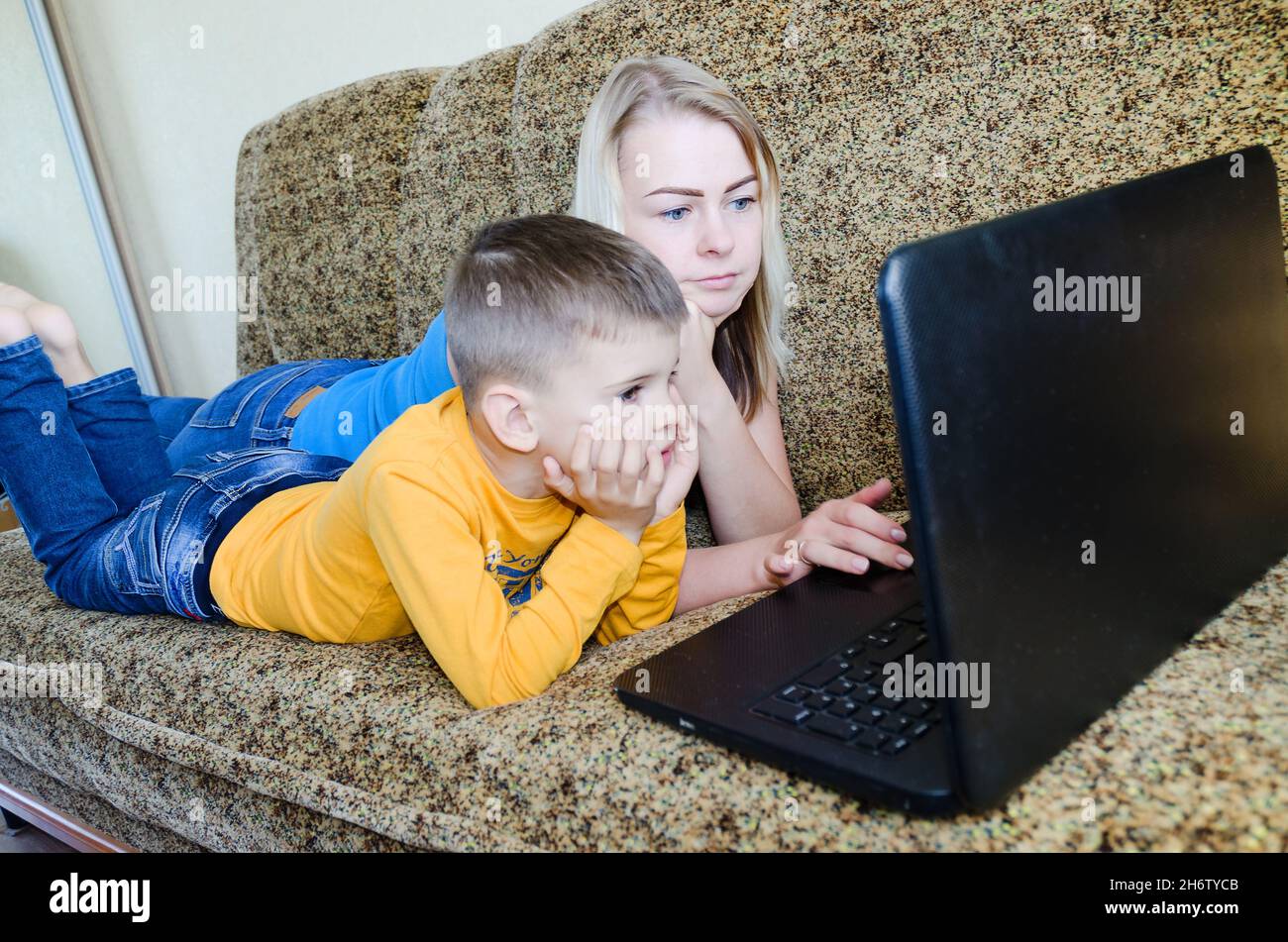 Madre e bambino piccolo stanco, ragazzo a casa seduto sul divano, usando il computer portatile, rilassarsi. Lavorare da casa. Buon stile di vita familiare, hobby, tempo libero. Affari Foto Stock