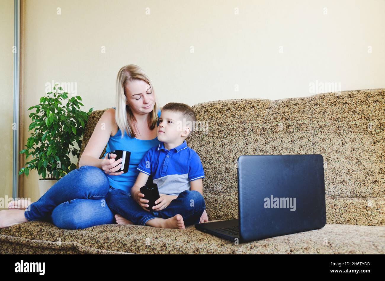 Madre e bambino piccolo stanco, ragazzo a casa seduto sul divano, usando il computer portatile, rilassarsi. Lavorare da casa. Buon stile di vita familiare, hobby, tempo libero. Affari Foto Stock