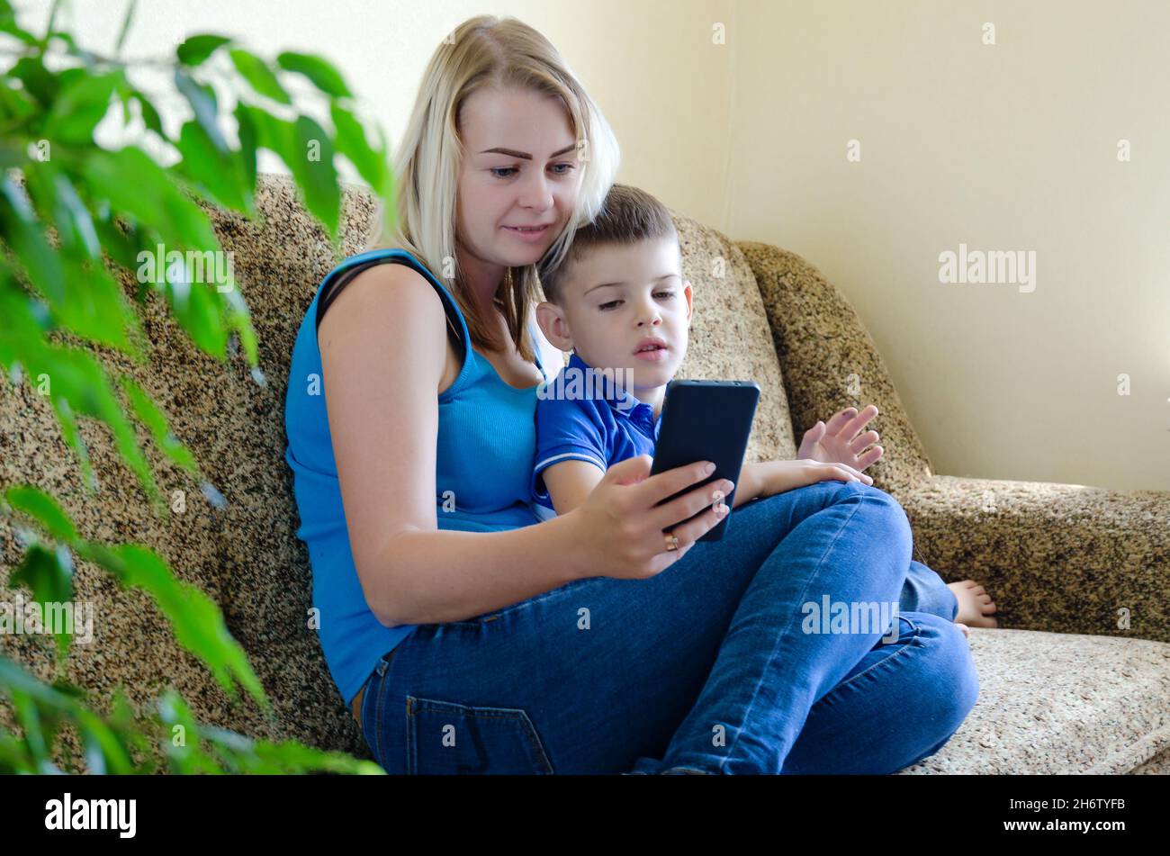 Madre e bambino piccolo stanco, ragazzo a casa seduto sul divano, usando il computer portatile, rilassarsi. Lavorare da casa. Buon stile di vita familiare, hobby, tempo libero. Affari Foto Stock