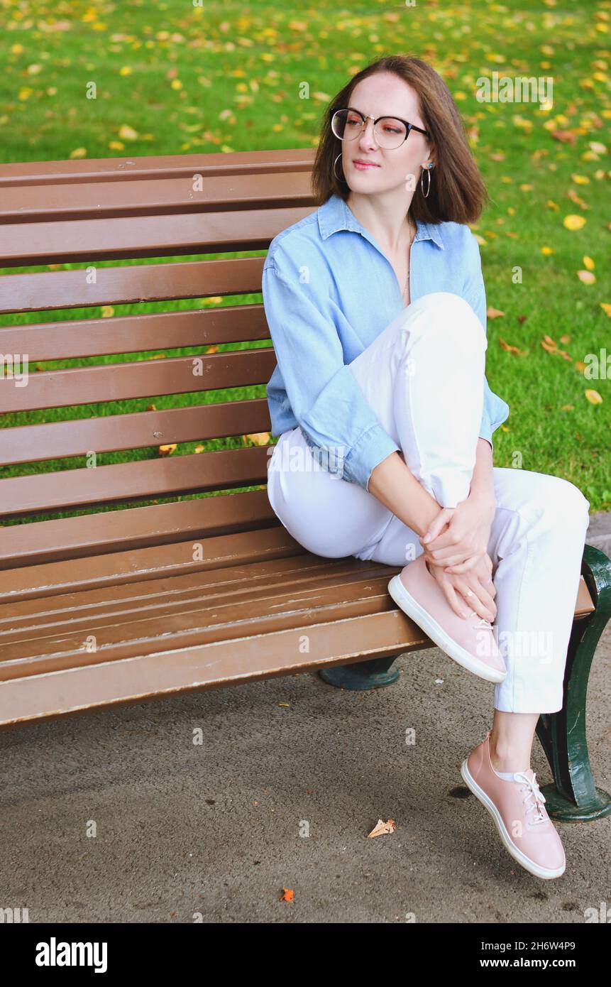 Ritratto urbano di giovane donna elegante in occhiali e abiti casual. Donna che cammina nella strada della città vicino alla fontana, rilassante, sorridente Foto Stock