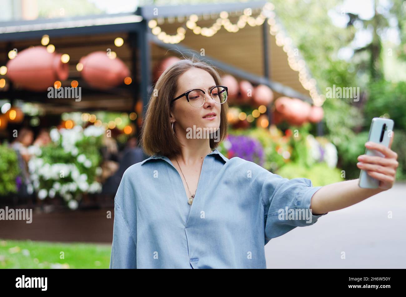Ritratto urbano di giovane donna elegante in occhiali e abiti casual. Donna che cammina nella strada della città vicino alla fontana, rilassante, sorridente Foto Stock