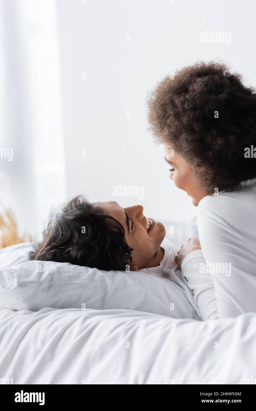 coppia interrazziale positiva sorridendo mentre si guarda l'un l'altro in camera da letto Foto Stock
