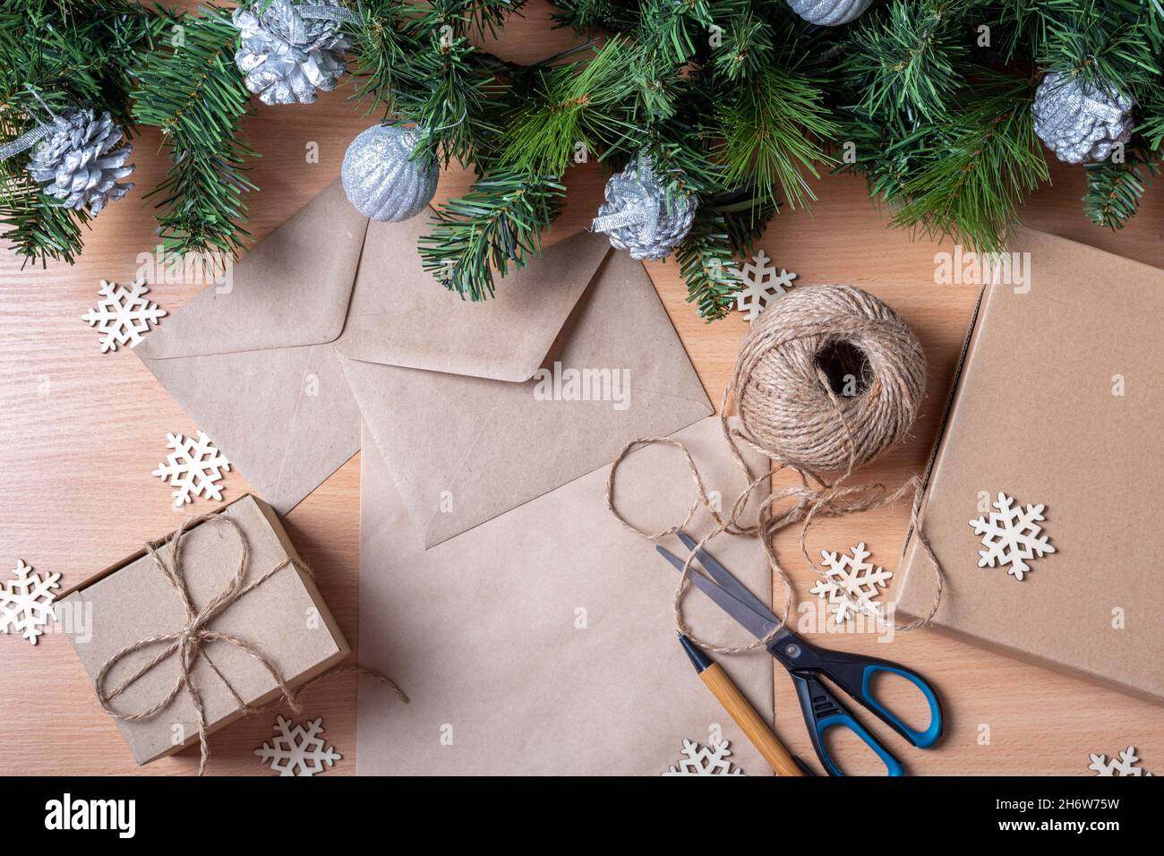 Concetto di Natale senza sprechi. Regali in scatole fatte a mano, carta riciclata, busta, spago, forbici, rami artificiali di abete rosso e fiocchi di neve di legno, a. Foto Stock