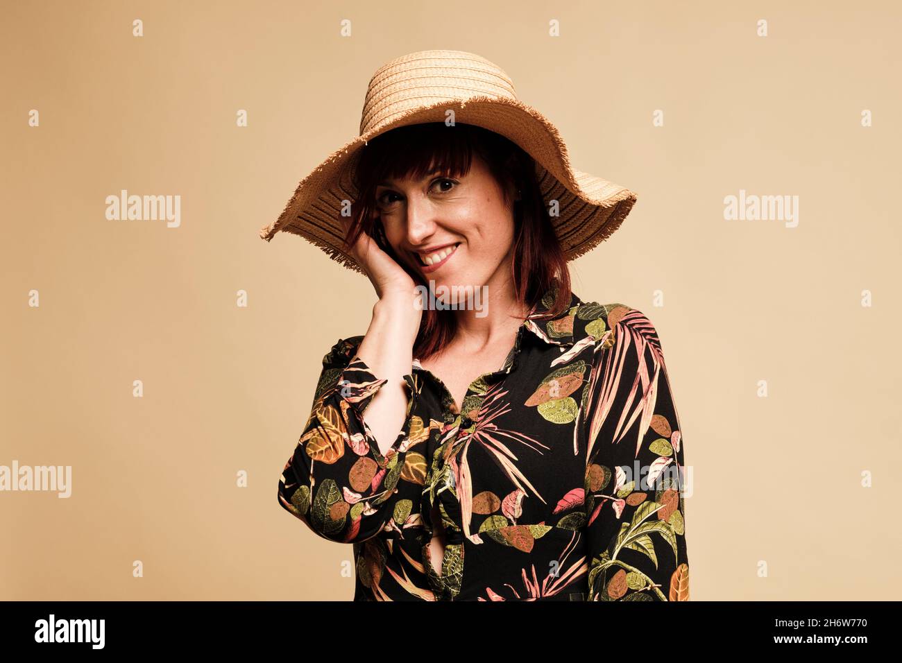 Bella donna rossa sorridente con un lungo abito floreale e cappello. Ritratto, con sfondo giallo. Foto Stock