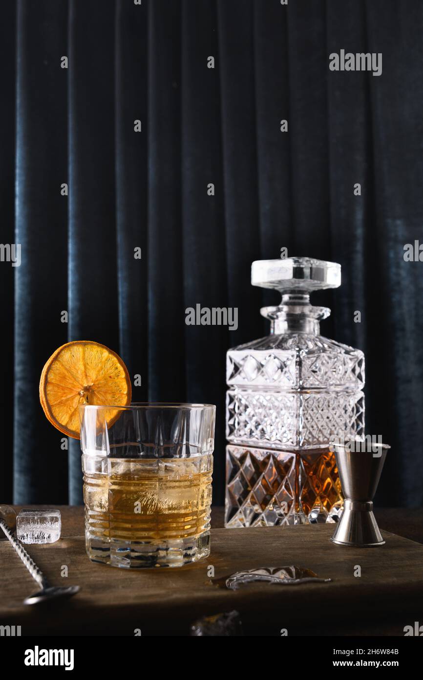 Il whiskey freddo nelle rocce guarnire le scaglie di arancio su uno sfondo di tenda blu scuro. Composizione verticale. Foto Stock