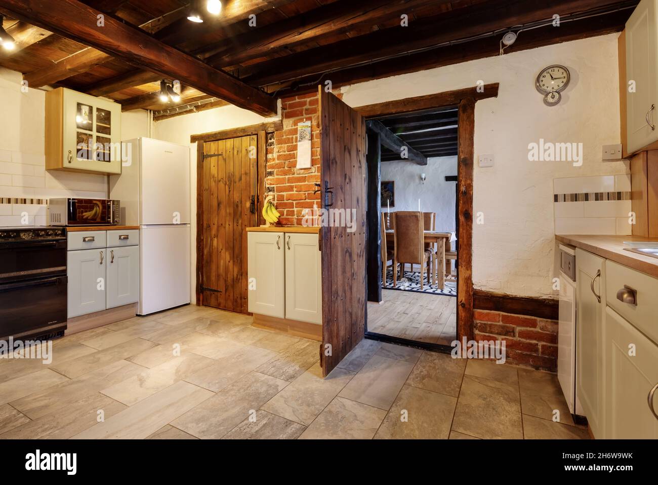 Kedington, Suffolk, novembre 19 2019: Cucina casolare scarsamente arredata con travi a vista e muro di mattoni. Porta aperta alla sala da pranzo. Foto Stock