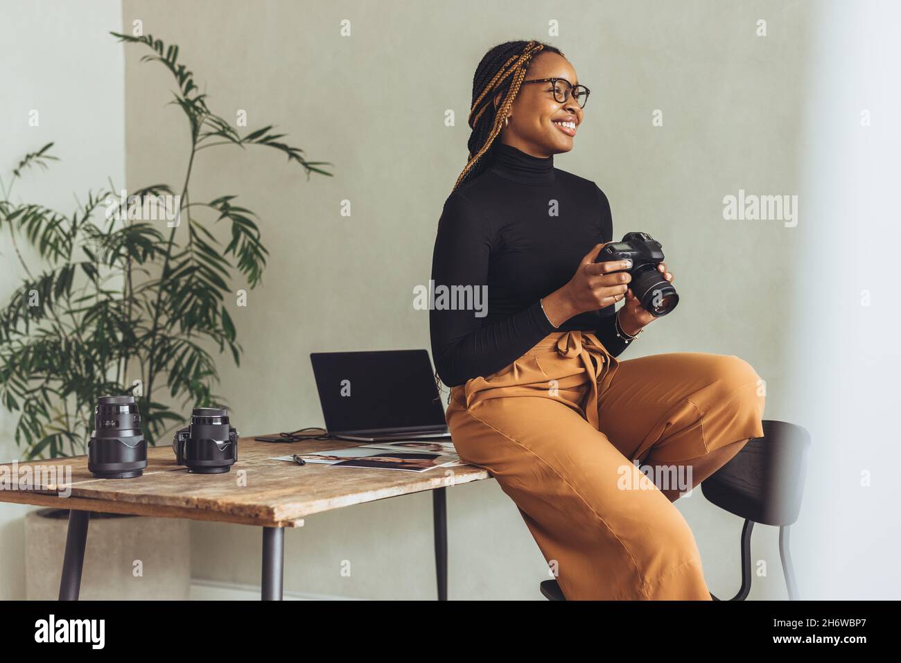 La felicità è un fotografo. Una libera creativa femminile sorride allegro mentre tiene una fotocamera dslr nel suo ufficio domestico. Fotografia giovane artistica Foto Stock