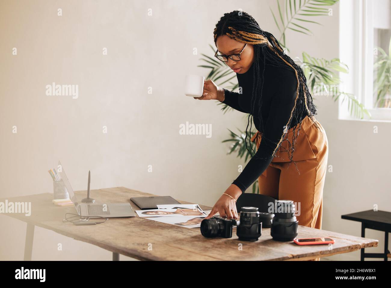 Giovane fotografo freelance che lavora con fotografie nel suo ufficio domestico. Giovane donna creativa in piedi su una scrivania con attrezzatura fotografica. Auto-em Foto Stock