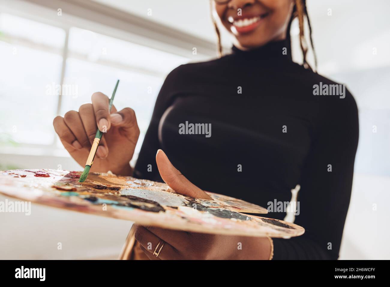Artista che tiene un pennello e una tavolozza nel suo studio d'arte. Felice pittore femmina sorridente allegro mentre si alza in casa sua studio. Female creativo Foto Stock