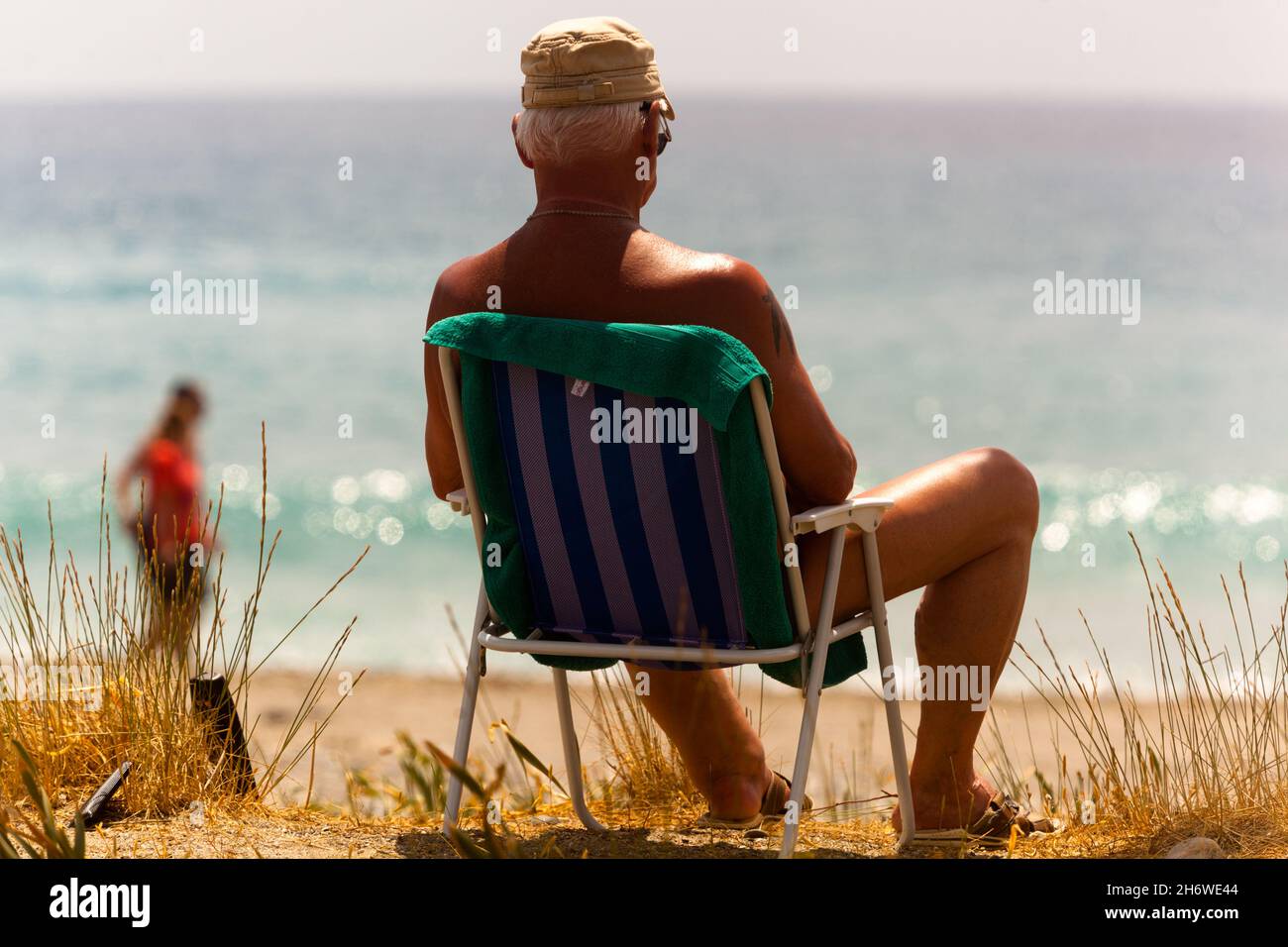 Uomo che prende il sole vacanza al mare, uomo anziano da solo, vista posteriore, che gode di calma sulla riva del mare in sedia a rotelle Foto Stock