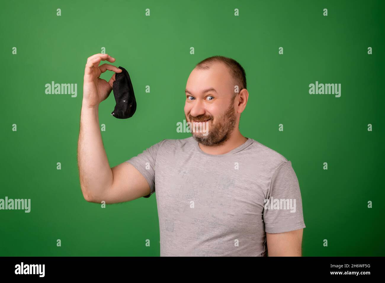 Un uomo di mezza età mostra un calzino sporco su uno sfondo verde. Lavanderia, igiene, concetto di piedi puzzolente. Foto Stock
