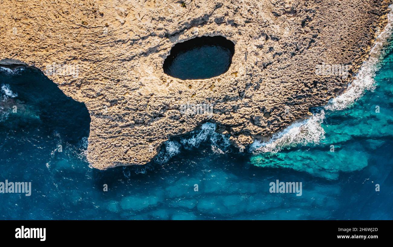 Vista aerea della grotta caduta di Ahrax, Laguna dei Coralli, Malta.Hole nel mezzo di rocce con acqua cristallina all'interno. Rocky costa maltese. Punto perfetto Foto Stock