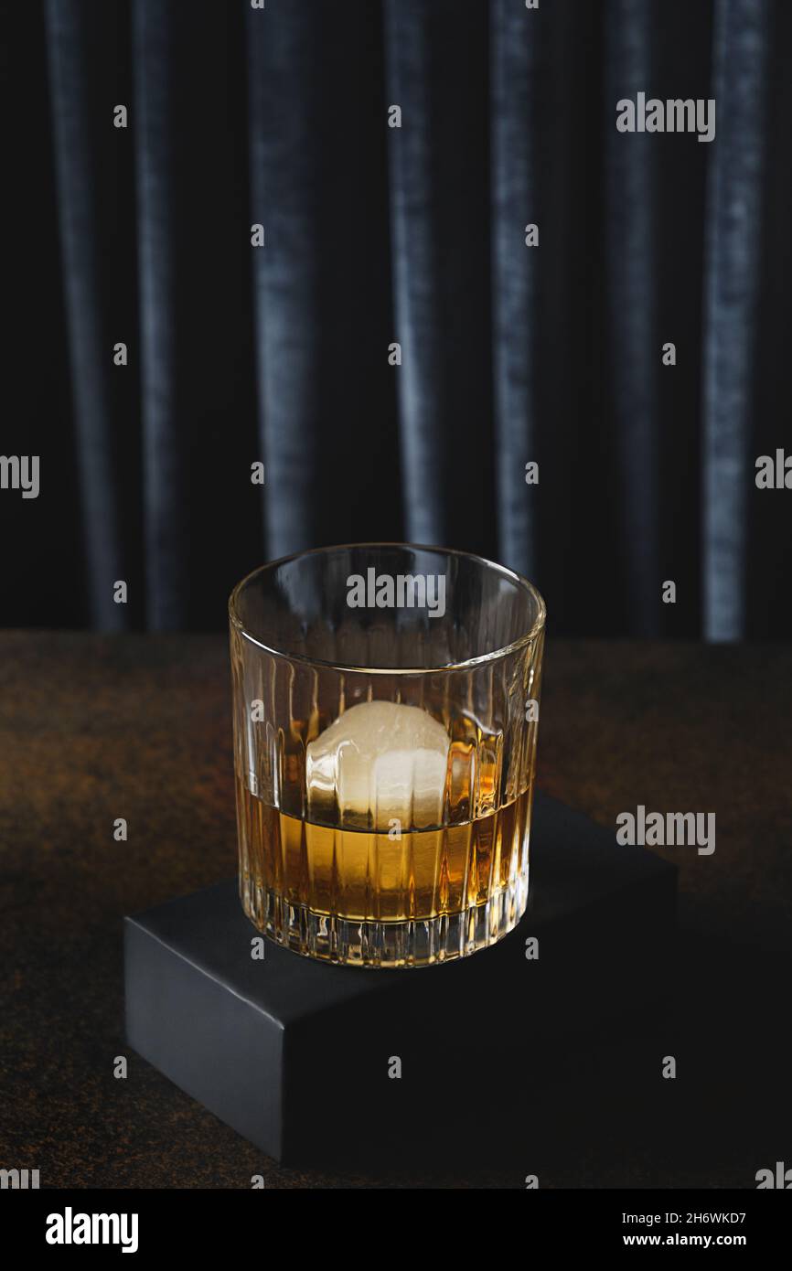 Whiskey freddo con ghiaccio o brandy in vecchio vetro di pietra fasion su sfondo scuro e moderno con podio. Foto Stock