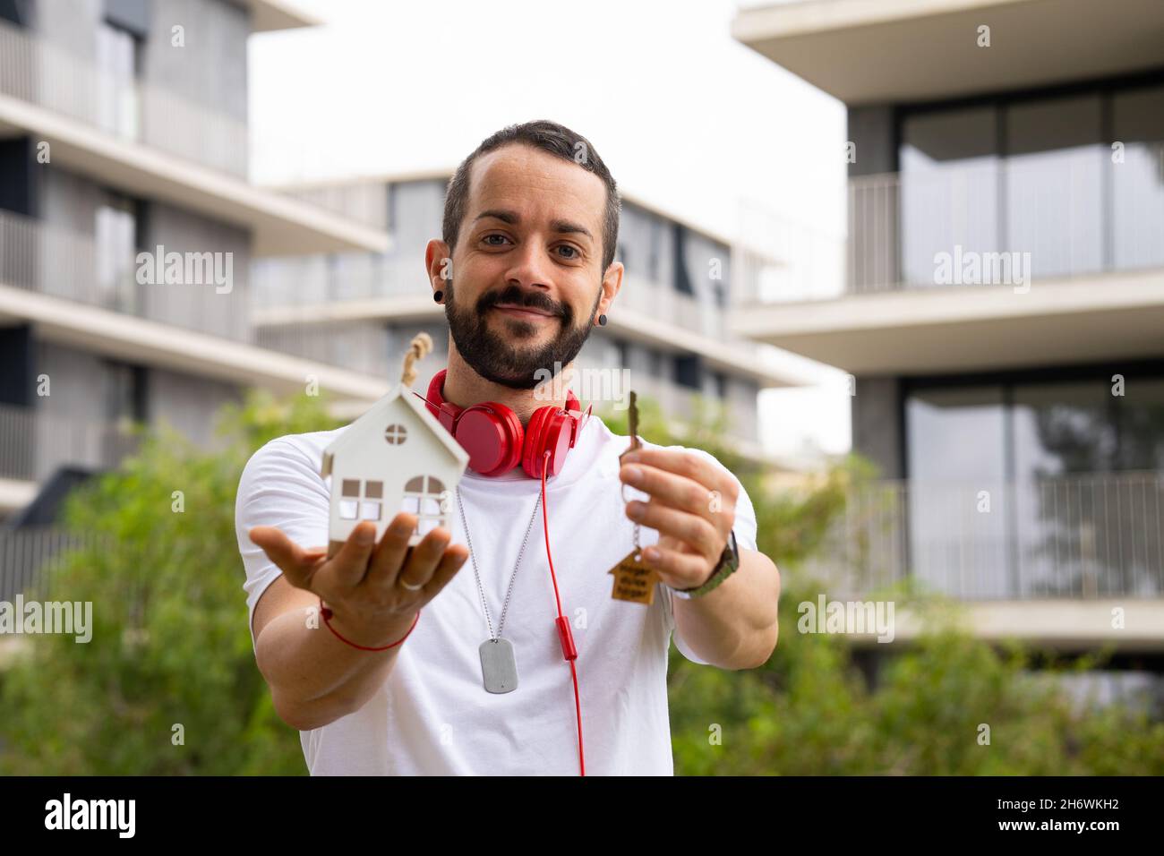 Giovane in posa con una chiave con portachiavi di mini casa e una casa in miniatura. Foto Stock