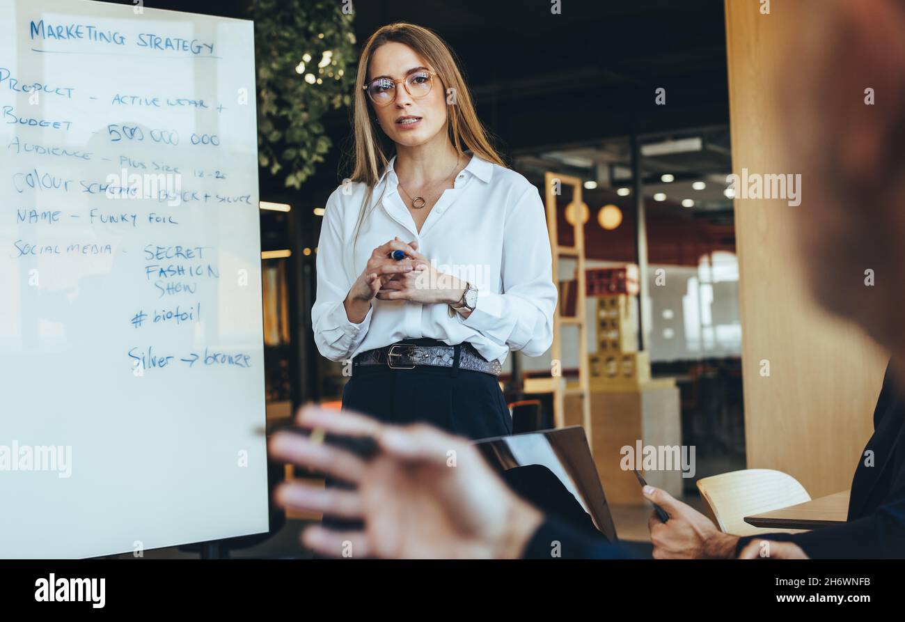 Giovane donna d'affari che discute le idee di vendita con il suo team in un ambiente di lavoro moderno. Fidato giovane manager aziendale che dà una presentazione durante un me Foto Stock