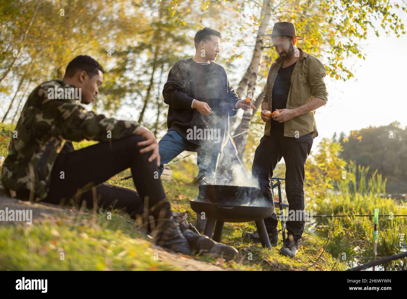 Amici maschi pesca e cucina sulla costa del lago Foto Stock