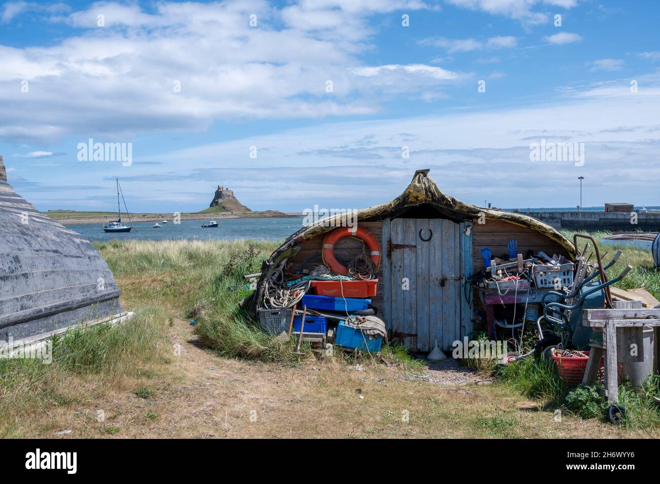 Attraenti 'capannoni' fatti da barche di aringa di legno ridiporto, il Porto di Lindisfarne, l'Isola Sacra. Il castello di Lindisfarne è sullo sfondo. Foto Stock