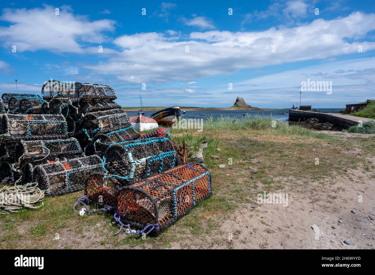 Porto di Lindisfarne, Isola Santa, con l'antico castello sullo sfondo e una serie di vasi di aragosta e barche. Foto Stock