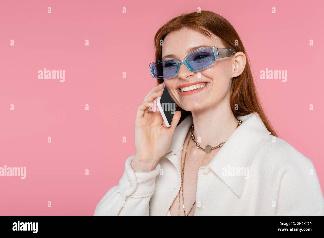 Elegante donna con capelli rossi in occhiali da sole che parlano su  smartphone isolato su rosa Foto stock - Alamy