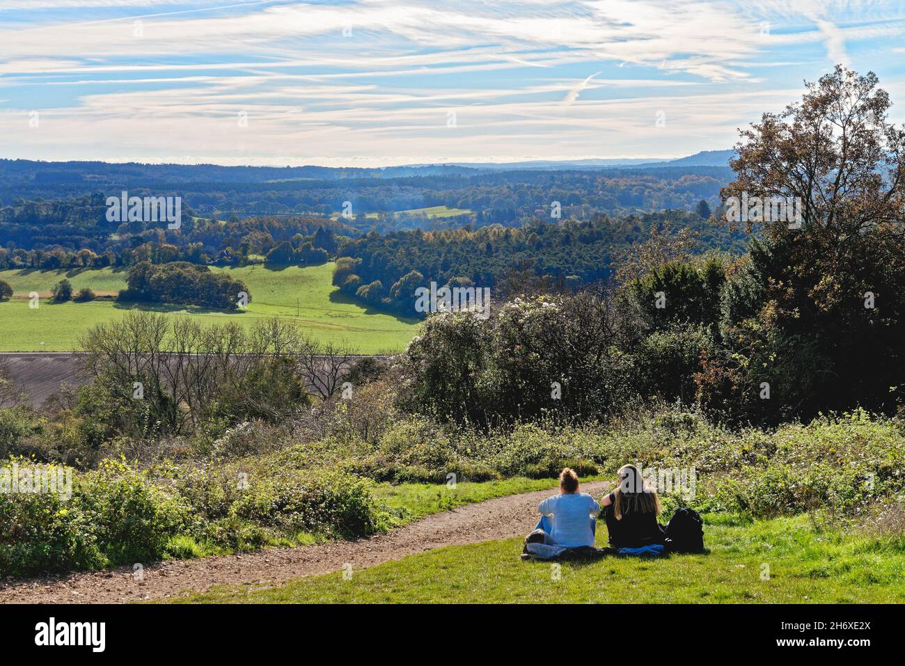 Due giovani ragazze seduti a terra al Newlands Corner guardando la vista della campagna del Surrey in una giornata d'autunno soleggiata vicino a Guildford Inghilterra UK Foto Stock