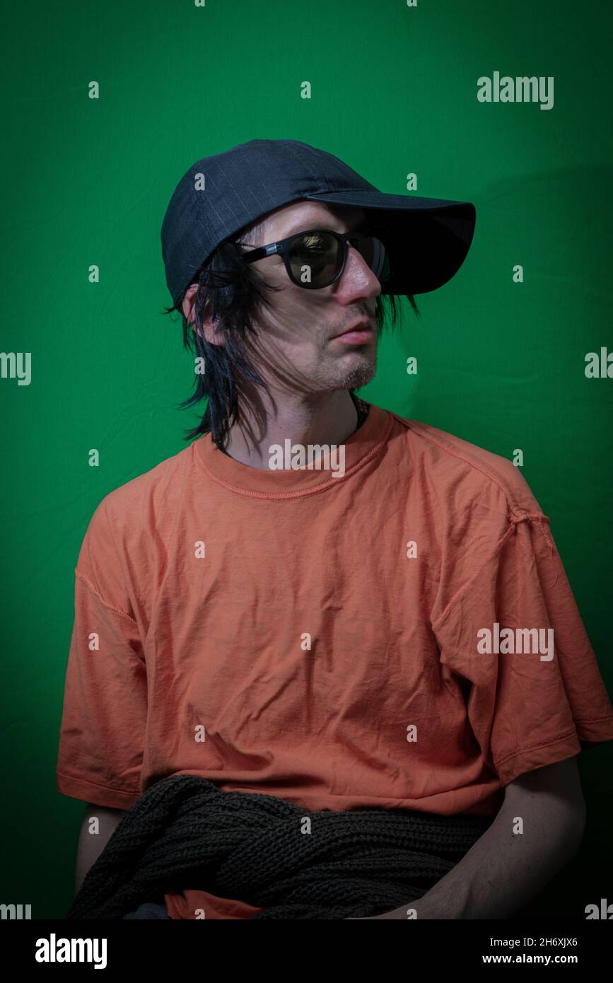 Uomo con capelli neri seduto vicino a una parete verde scuro Foto Stock