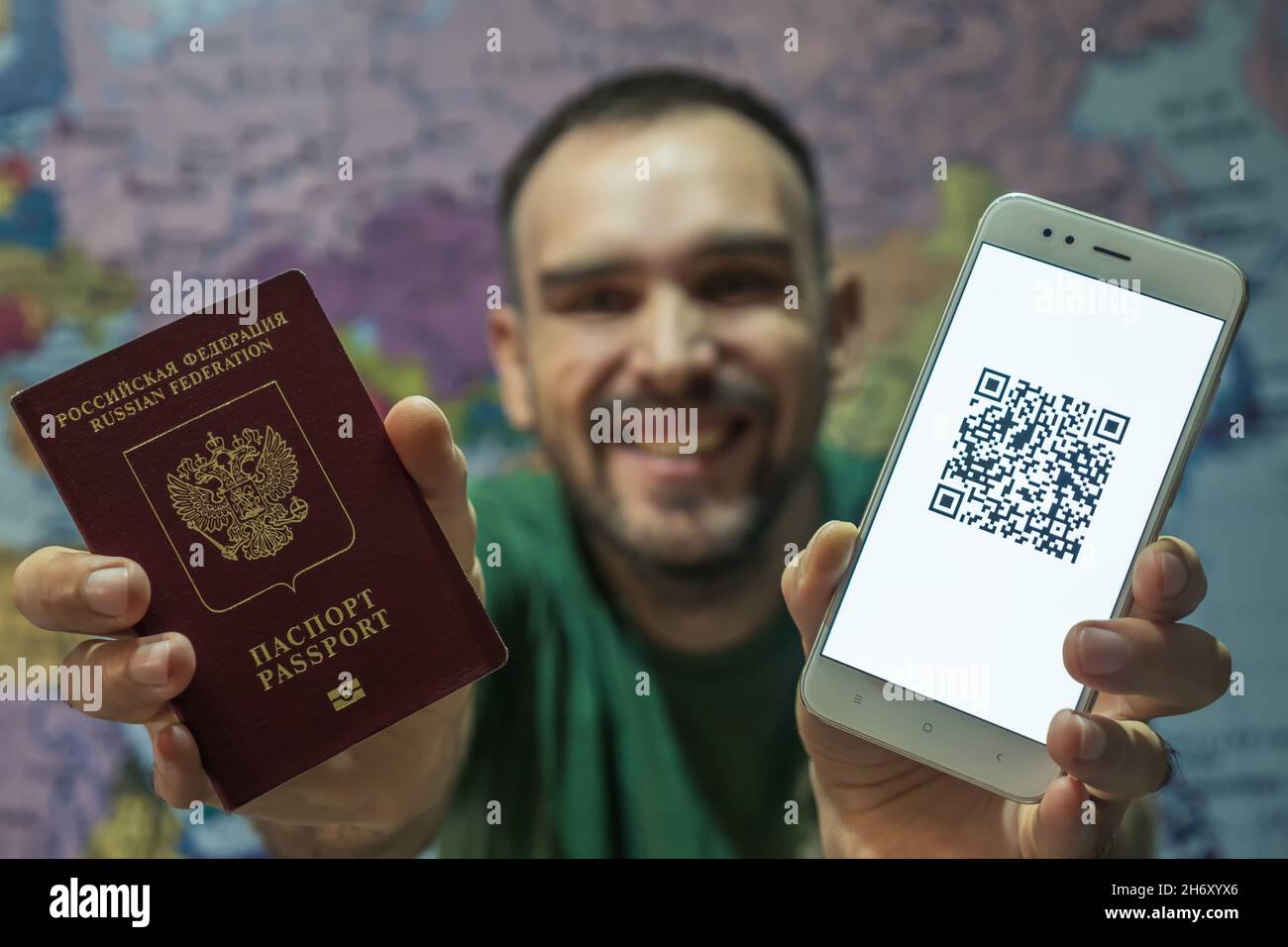 Un uomo gioioso in una T-shirt verde è in possesso di un passaporto e un telefono con un codice QR del codice di vaccinazione digitale covid-19 sullo schermo. Elettr Foto Stock