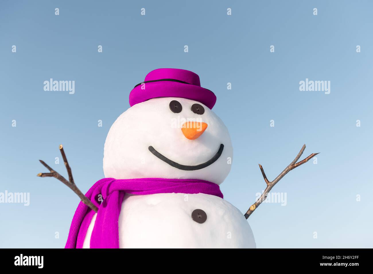 Divertente pupazzo di neve in elegante cappello marrone e cuoio capelluto rosa su campo nevoso. Cielo blu sullo sfondo Foto Stock