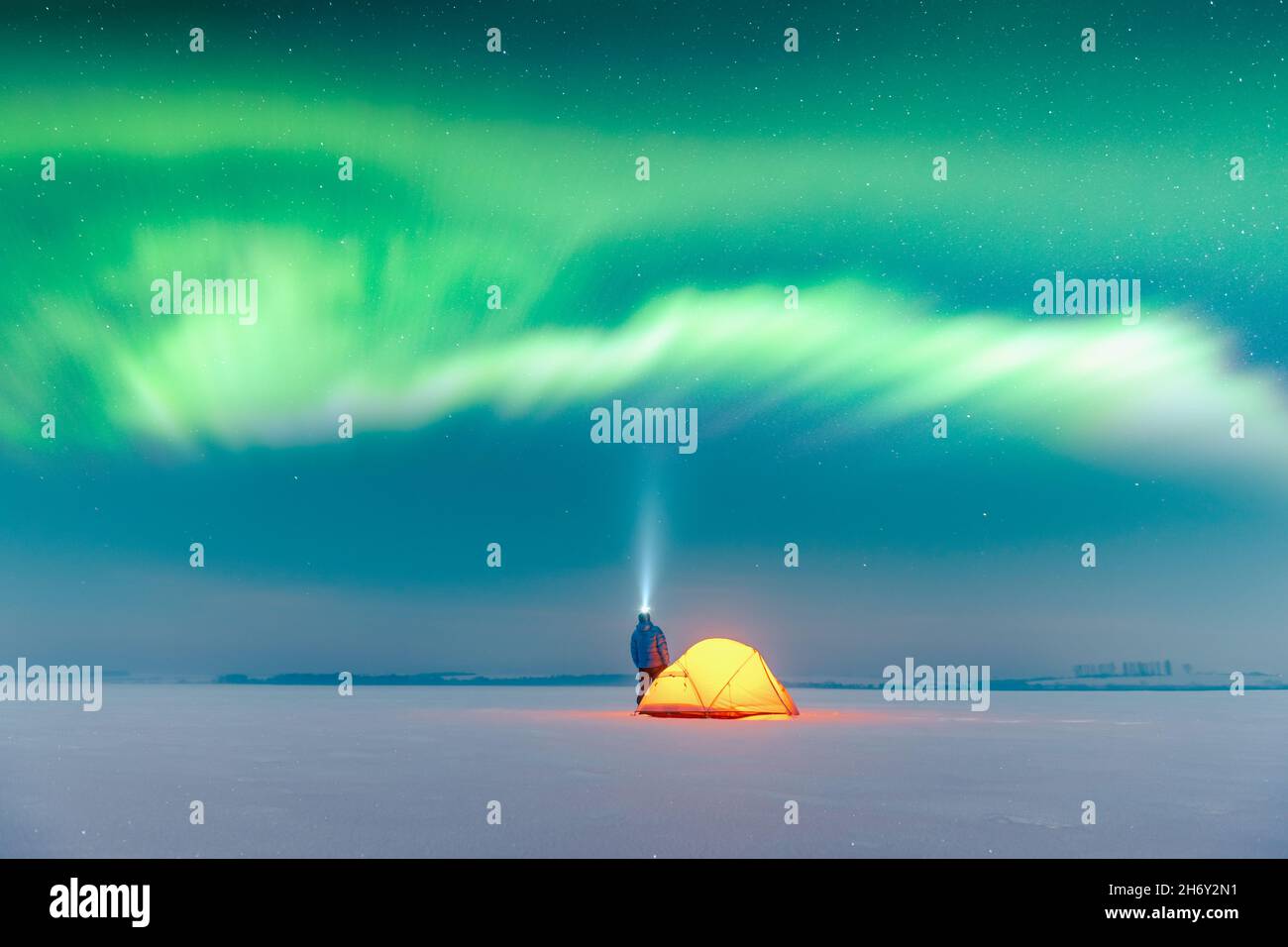 Turista con torcia vicino tenda gialla illuminata dall'interno contro lo sfondo di incredibile cielo stellato con Aurora borealis. Panorama notturno incredibile. Aurora boreale in campo invernale Foto Stock
